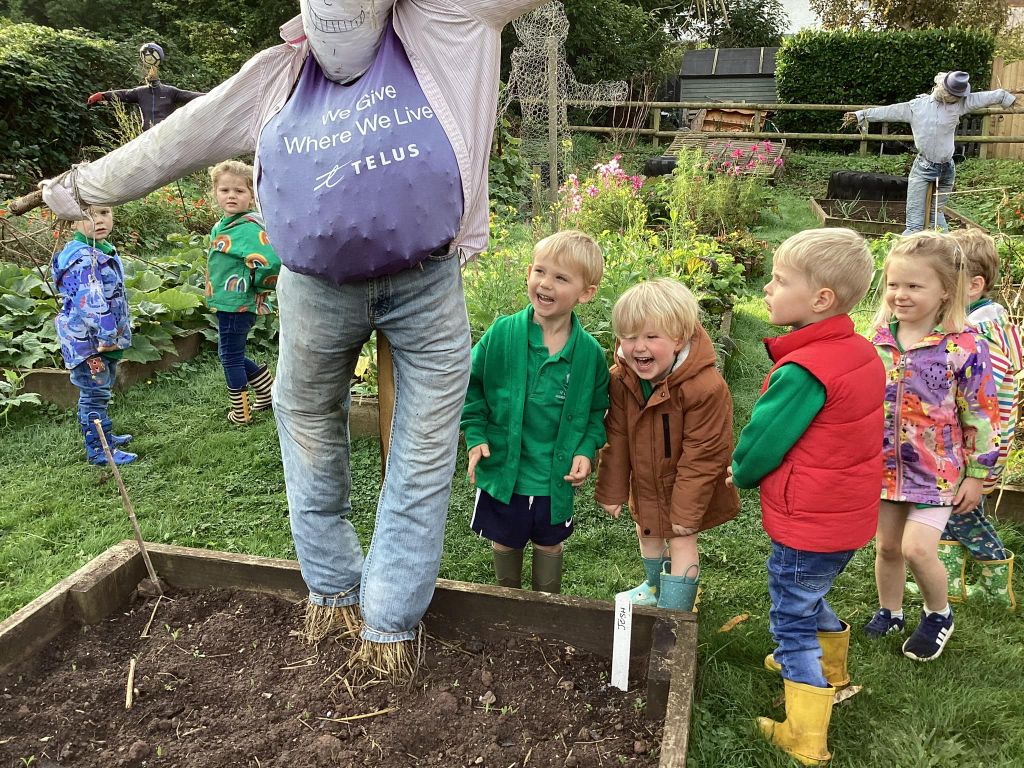 Children laughing at a scarecrow in a garden